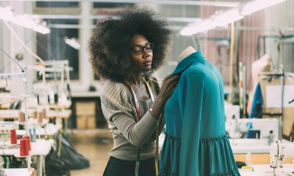 Mulher negra mexendo em peça de roupa no manequim