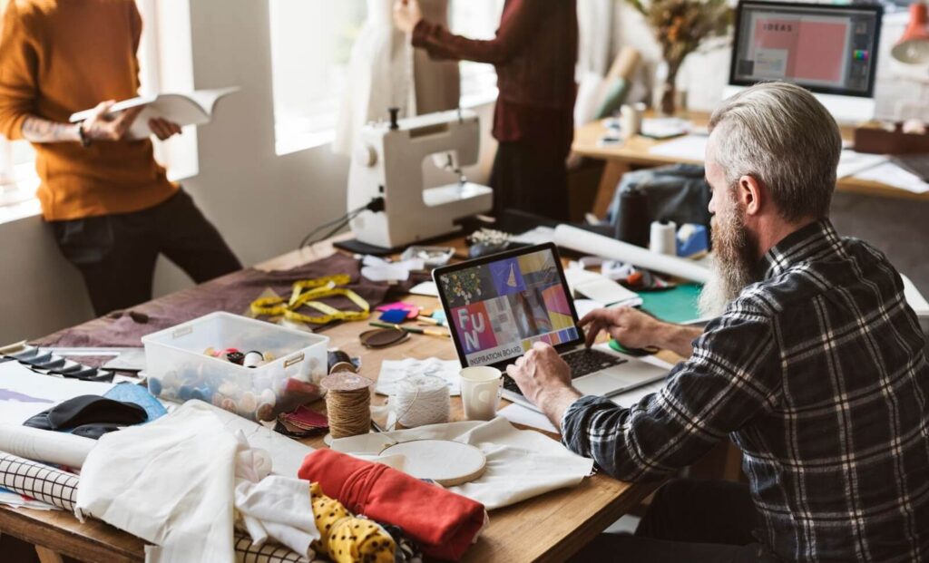 Homem mexendo no compuador em ateliê de roupas